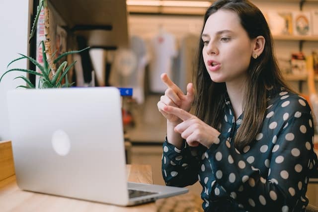 An independent woman is at her laptop speaking and gesturing as she manages her projects remotely.