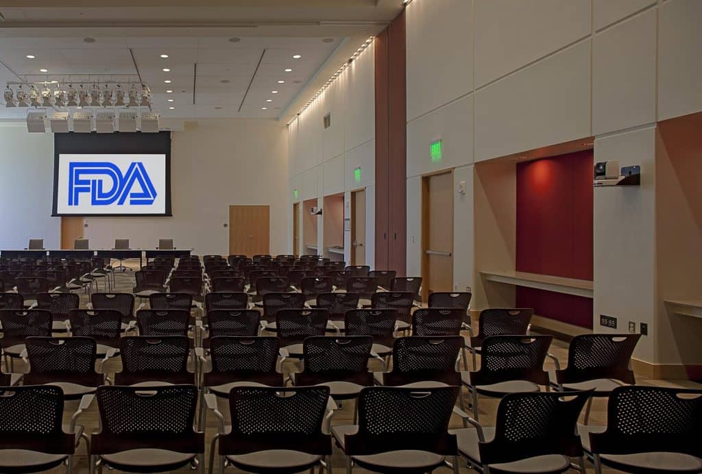 A conference room with many rows of seats and a screen at the front on which a large image of the FDA logo is projected.