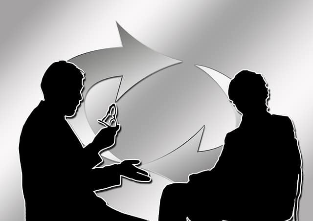 Two clinical operations consultants evaluating feedback and monitoring. They are both shown in silhouette with large arrows in the background representing a feedback loop.