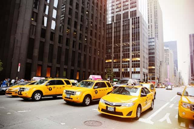 Ground transportation waiting for independent consultants. Yellow taxis can be seen lined up next to each other on a street. High rise buildings are in the background.